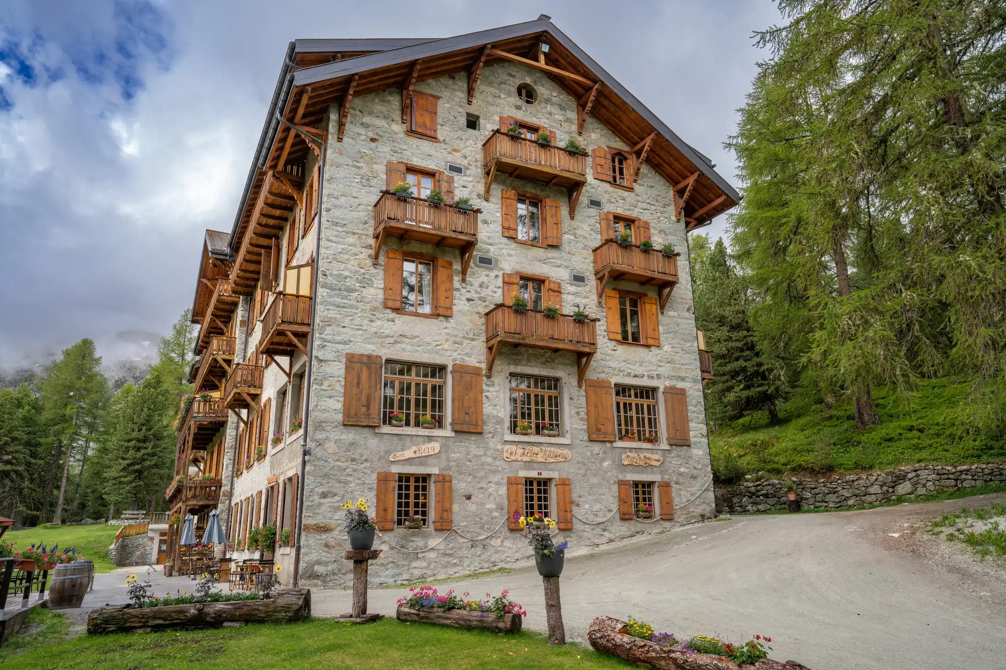 La façade en pierre du Grand Hôtel & Kurhaus en été, balcons fleuris et forêt d'arolles — Arolla, Val d'Hérens, 2 070 m